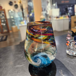 A multicolored glass with wave patterns displayed on a table, likely made of glass and metal.