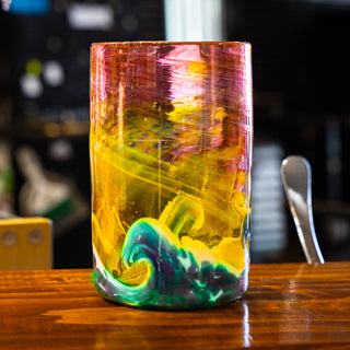 Colorful handmade Lake Superior ARt Glass tumbler with a wave design on a wooden surface
